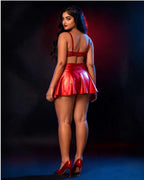 A woman posing from behind wearing a shiny red two-piece outfit consisting of a crop top and a pleated mini skirt, paired with red high heels, set against a dark studio background with red and blue lighting.