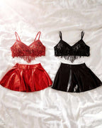 Two two-piece outfit sets laid flat on a white wrinkled fabric background. The left set is red, featuring a red sequined fringe crop top and a shiny red mini skirt.