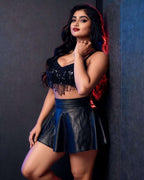 A woman posing in a black sequined fringe crop top and a black faux-leather mini skirt against a dark textured wall.
