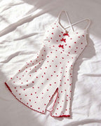 White ribbed knit camisole dress with small red heart print, red bow details at the neckline, and red scalloped trim, laid flat on a white fabric background.