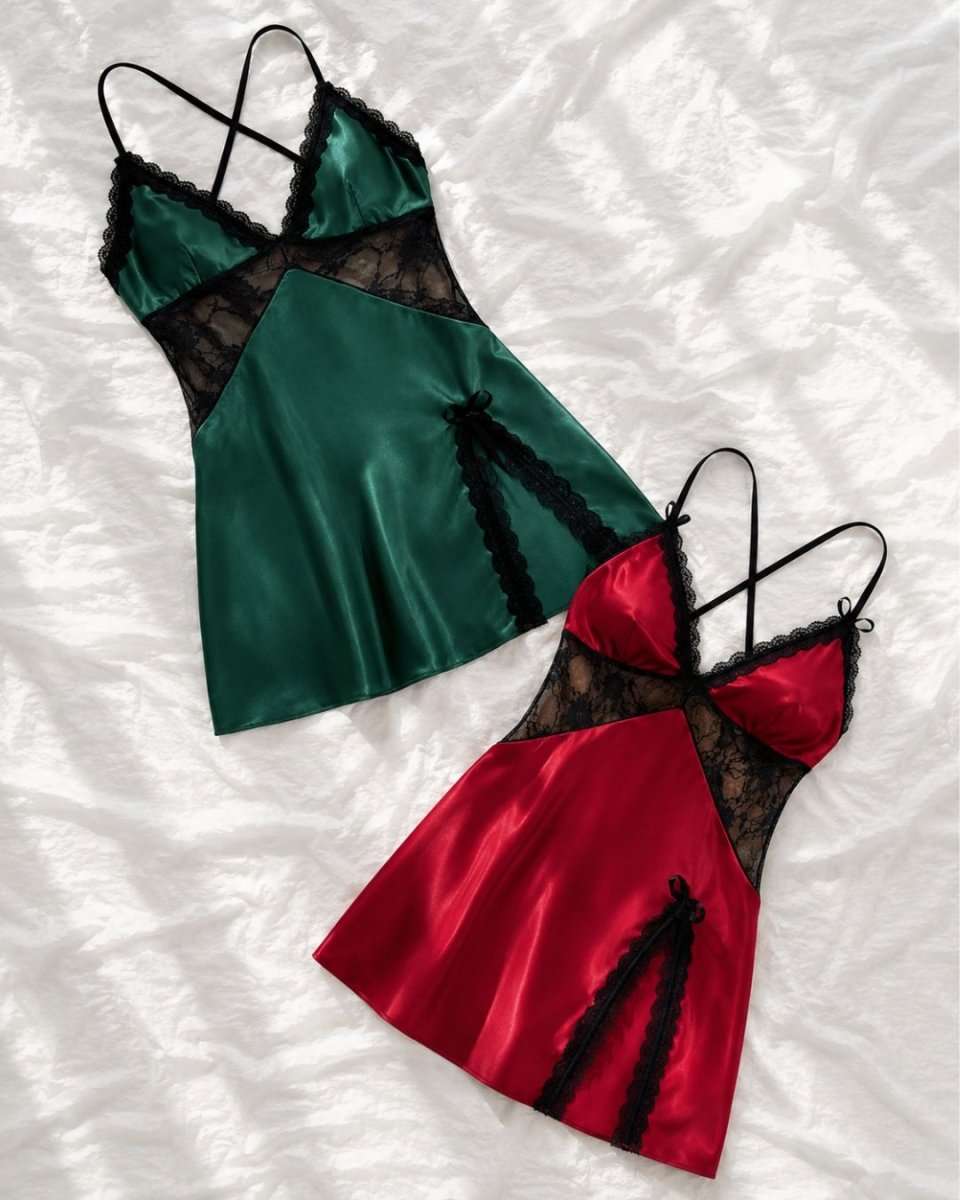 Two satin babydoll chemises laid flat on a white textured fabric background. One is emerald green with black lace panels and trim, and the other is bright red with black lace panels and trim.