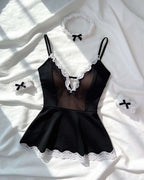 Black lingerie bodysuit with white lace trim and matching accessories, laid flat on white fabric with soft shadows.