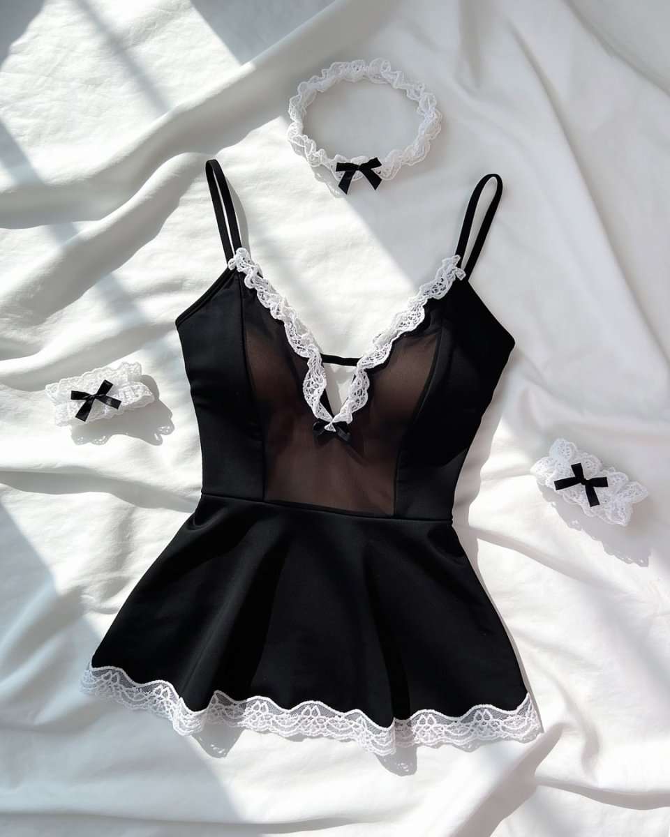 Black lingerie bodysuit with white lace trim and matching accessories, laid flat on white fabric with soft shadows.