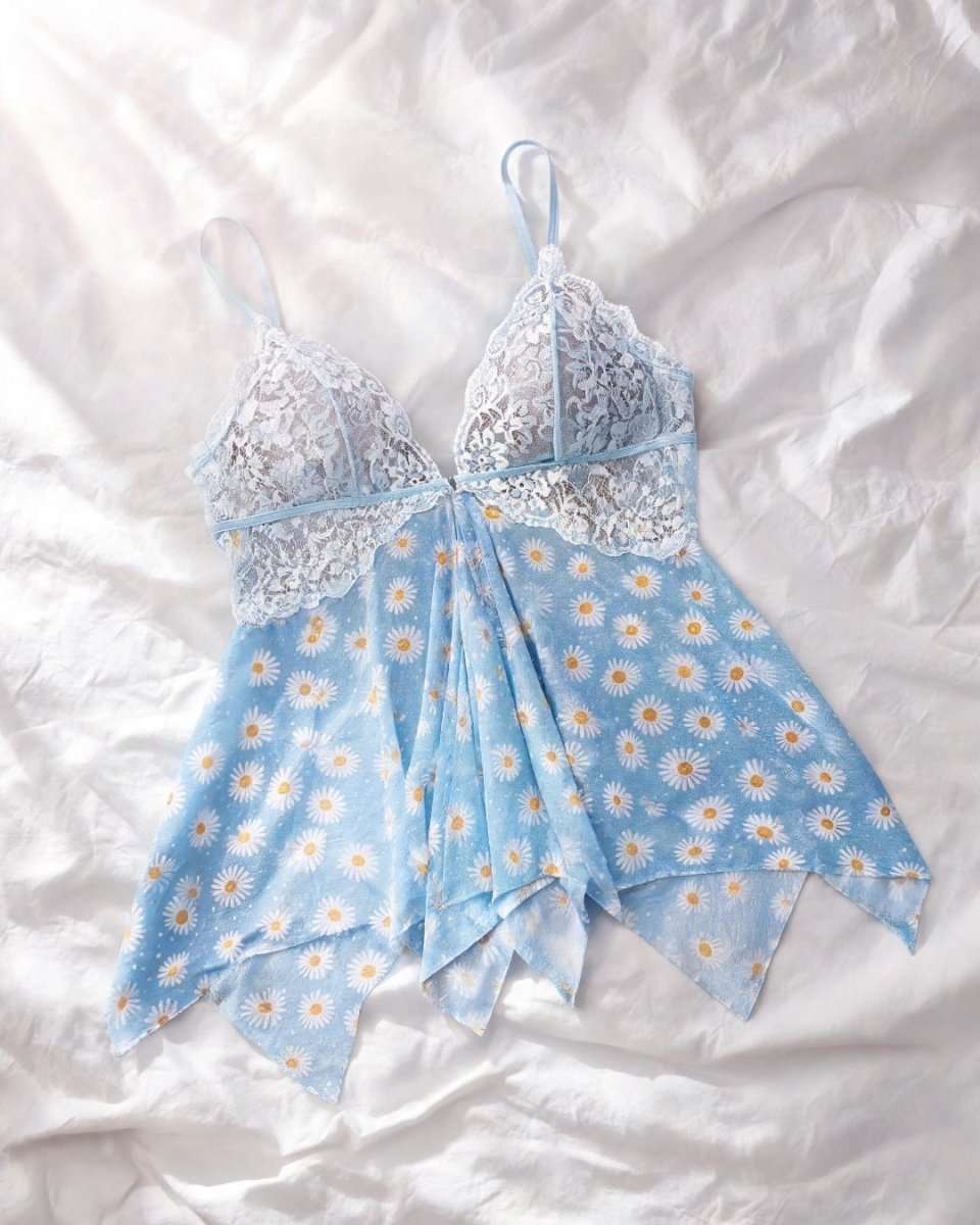 A light blue babydoll lingerie dress with a daisy print and lace cups, laid flat on a white fabric background.