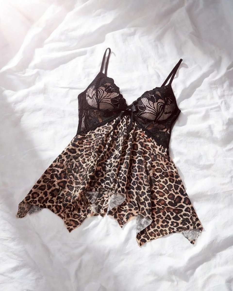 A sheer lingerie chemise laid flat on white bedding, featuring a dark brown floral lace bodice and a leopard print skirt.