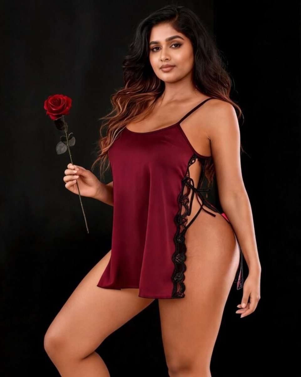 A woman modeling a burgundy satin slip-style lingerie chemise with black lace trim and side ties, holding a red rose against a black studio background.