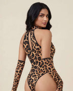 A woman modeling a leopard-print bodysuit with matching long sleeves, shown from a rear three-quarter angle against a plain beige studio background.