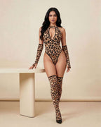 A woman modeling a leopard-print halter bodysuit with matching thigh-high stockings and black heels, standing beside a minimalist beige table against a neutral beige studio backdrop.