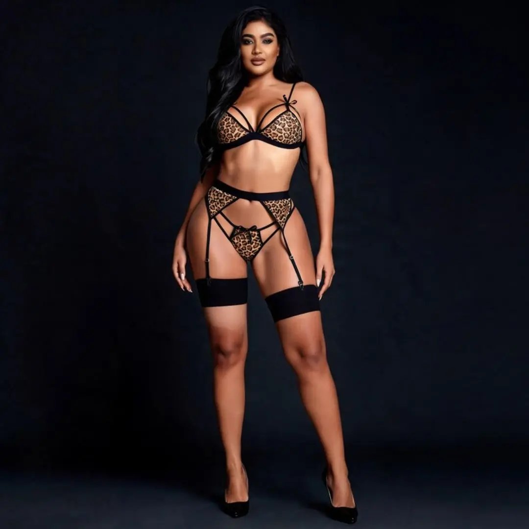 A woman modeling a black lace lingerie set with leopard-print panels, including a bra, garter belt, panty, and thigh-high garter straps, against a dark studio background.